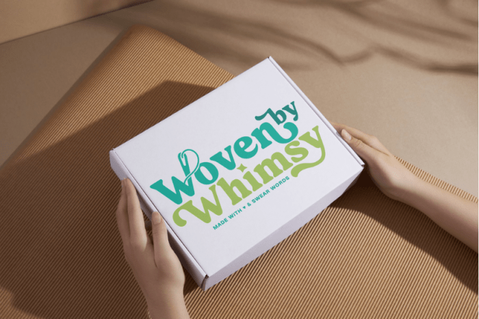 hands holding white box with "Woven by Whimsy" text on the front in blue and green hues against brown background